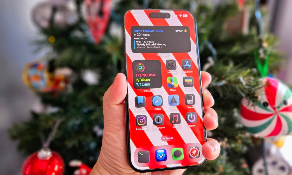 iPhone 15 Pro held in hand in front of a Christmas tree.