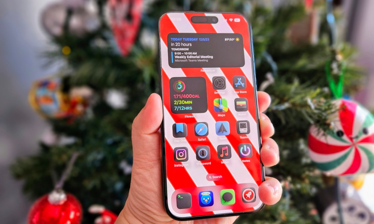 iPhone 15 Pro held in hand in front of a Christmas tree.