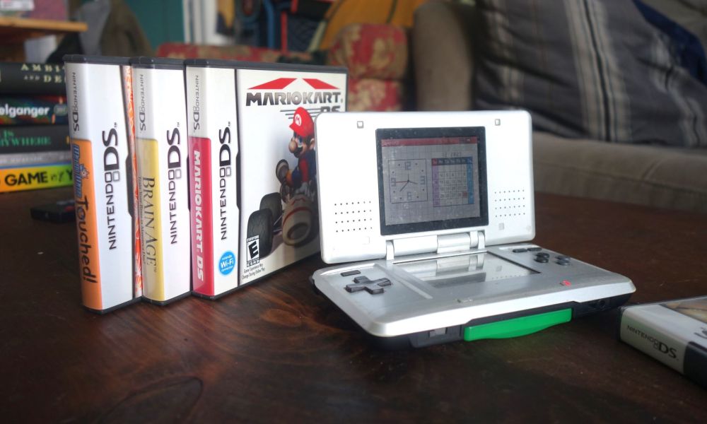 A Nintendo DS sits on a table with a few game boxes.