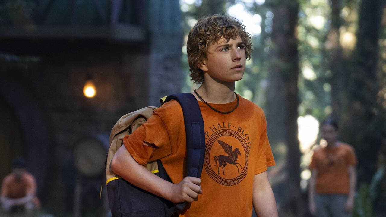 Percy en Percy Jackson y los atletas olímpicos de pie con una camiseta naranja y una mochila.