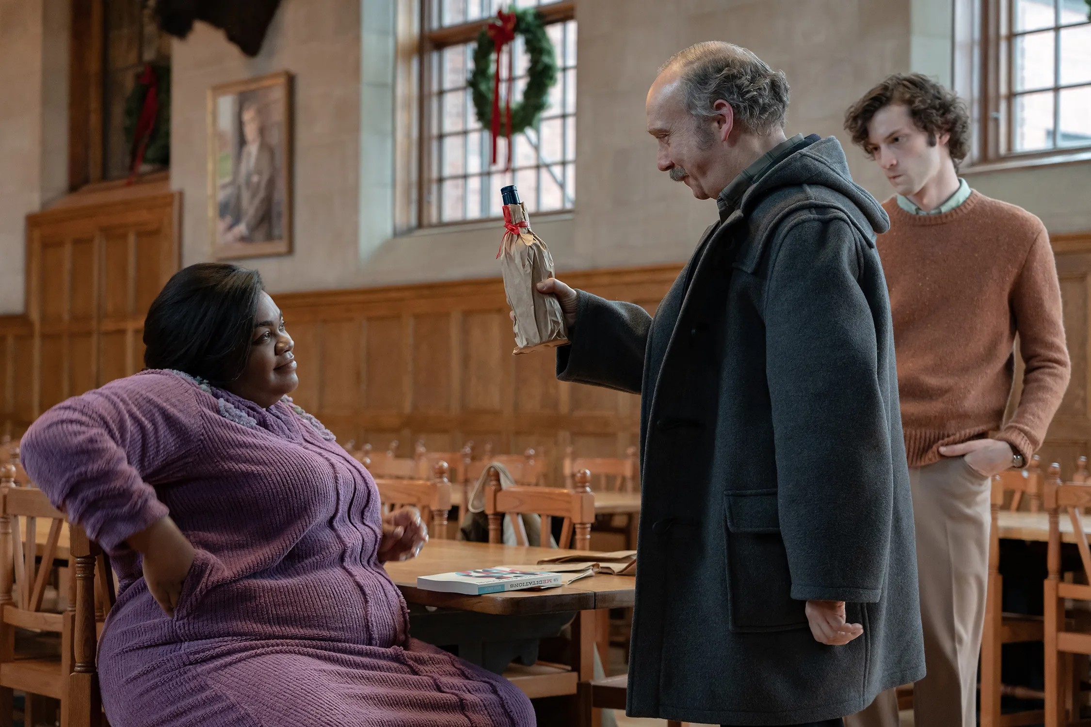 Ein Mann hält eine Flasche in der Hand, während zwei andere in „The Holdovers“ zuschauen.