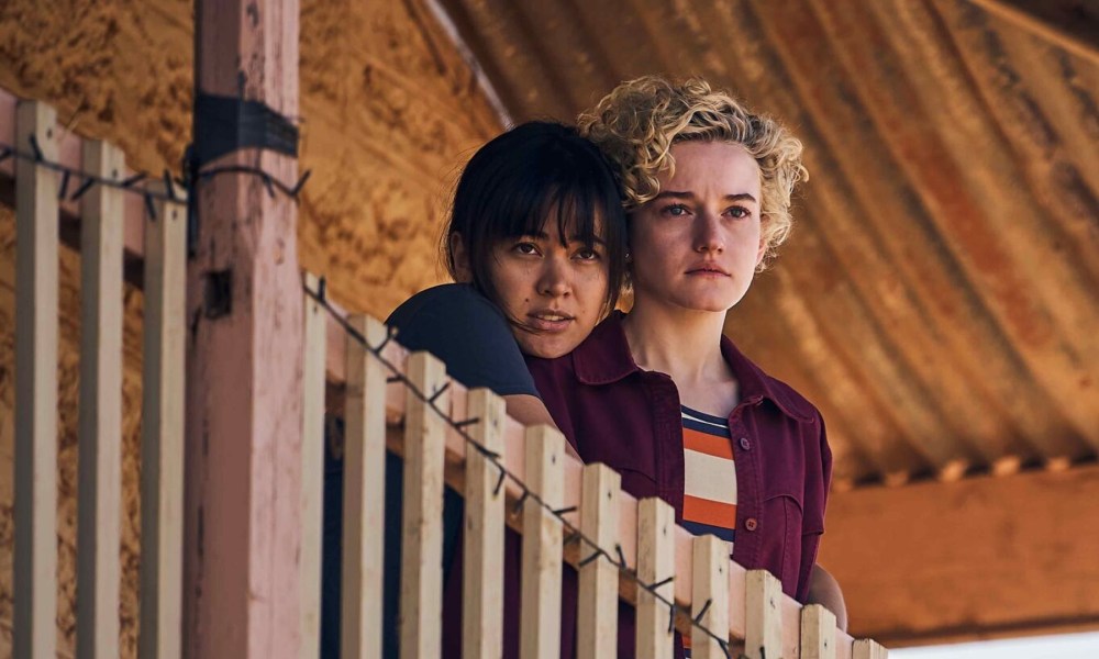 Jessica Henwick and Julia Garner hug and look out over a balcony in a still from the movie The Royal Hotel