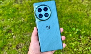 OnePlus 12 Flowy Emerald held in hand against grass background.