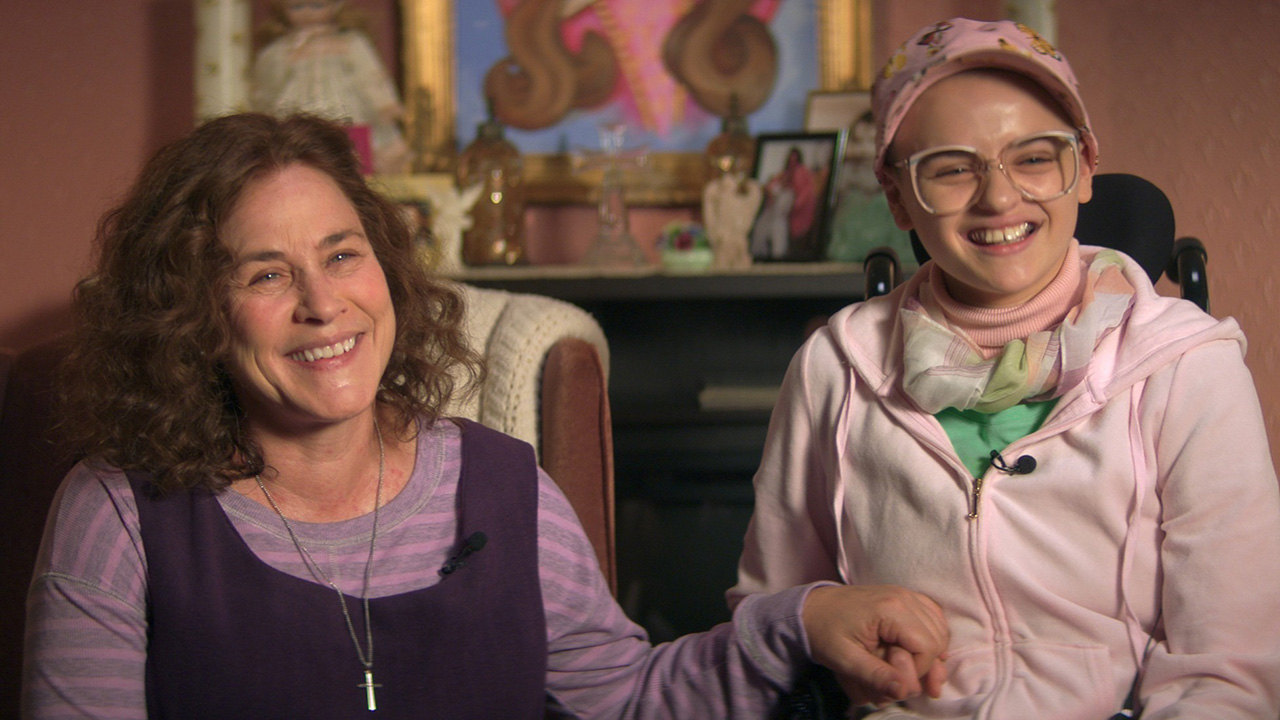 Patricia Arquette e Joey King como Dee Dee e Gypsy Blanchard, sentados juntos de mãos dadas em uma cena de The Act.