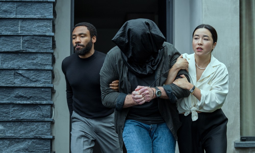 Donald Glover and Maya Erskine drag a man with a bag over his head together in Mr. & Mrs. Smith.