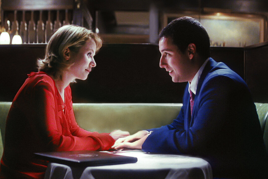 Emily Watson e Adam Sandler sentam-se juntos em uma mesa em Punch-Drunk Love.