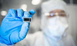 An Intel Foundry employee holds a chip between fingertips.