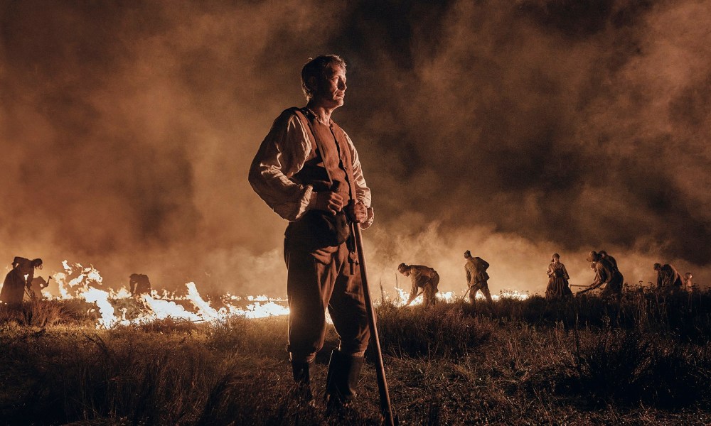 Mads Mikkelsen stands near a burning field in The Promised Land.