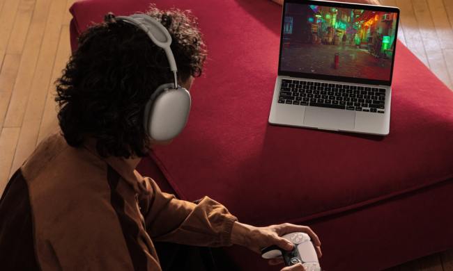 A person plays Stray using a PlayStation controller on a silver 13-inch MacBook Air.