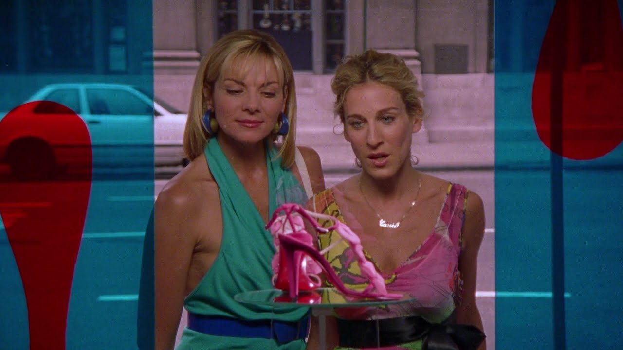 Kim Cattrall e Sarah Jessica Parker como Samantha e Carrie olhando para um par de sapatos através de uma janela em Sex and the City.