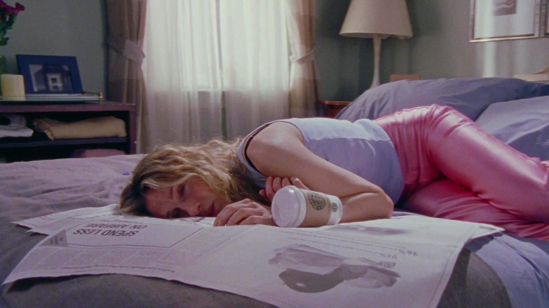 Sarah Jessica Parker como Carrie Bradshaw deitada em cima de um jornal em sua cama em Sex and the City.