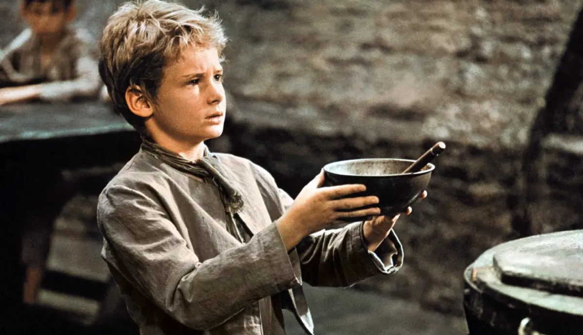 Un jeune garçon tient un bol dans ses mains dans Oliver !