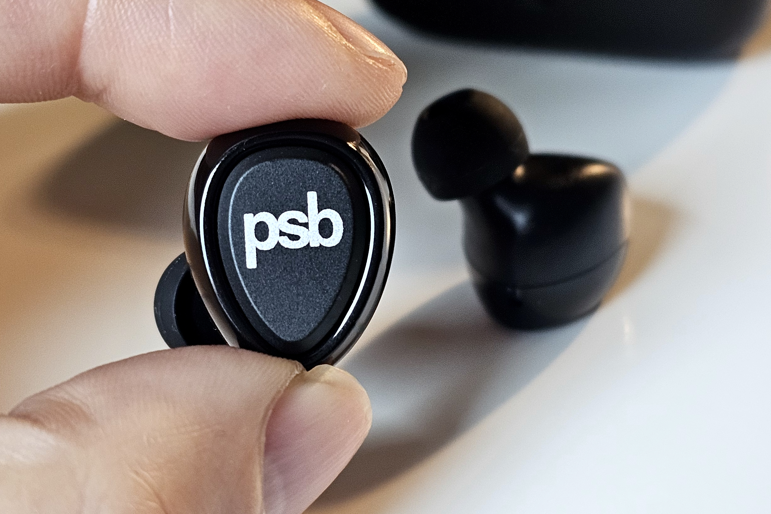 PSB Speakers M4U TWM left earbud held between a finger and a thumb.