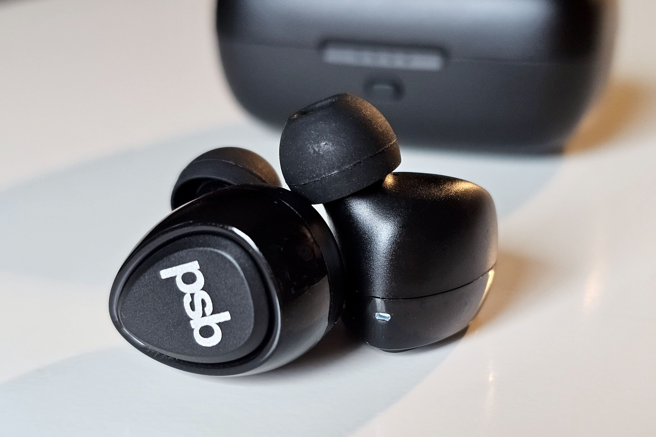 PSB Speakers M4U TWM earbuds in front of charging case.