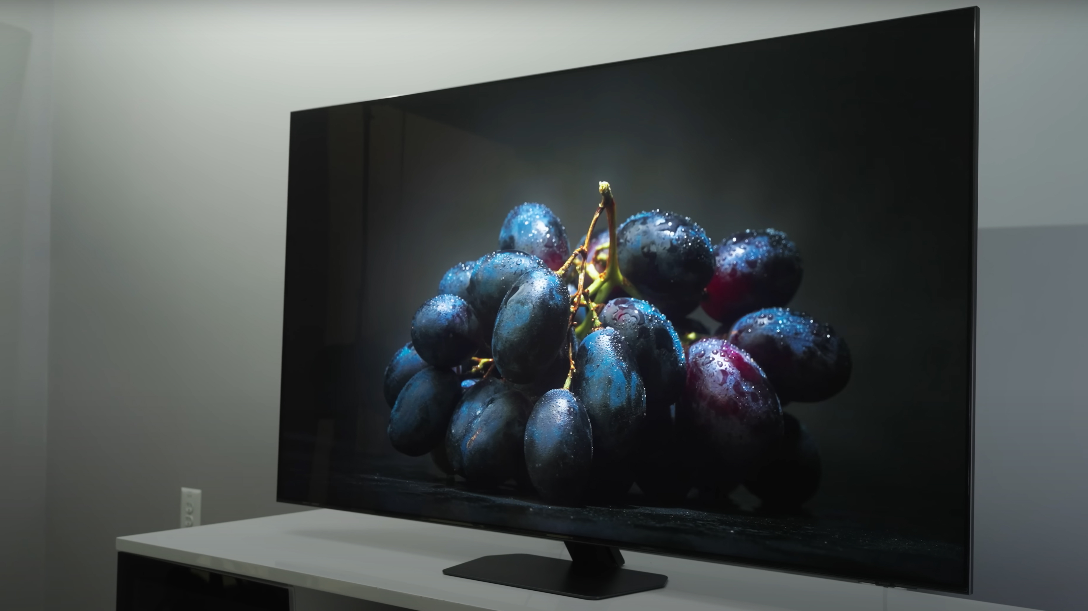 A closeup of moodily lit dark purple grapes on a black background shown on a Samsung QN90D.