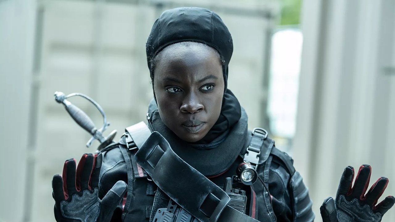 Michonne dans un uniforme CRM, son casque retiré et les mains en l'air dans une scène de The Walking Dead : The Ones Who Live.