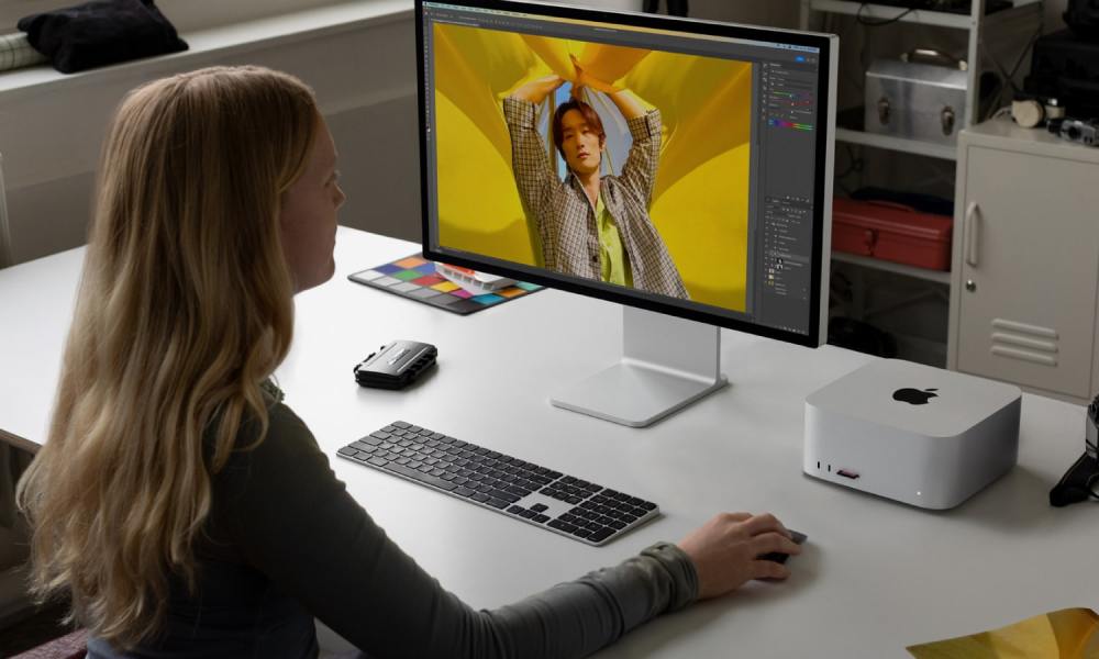 A person uses an Apple Mac Studio and a Studio Display monitor at a desk.