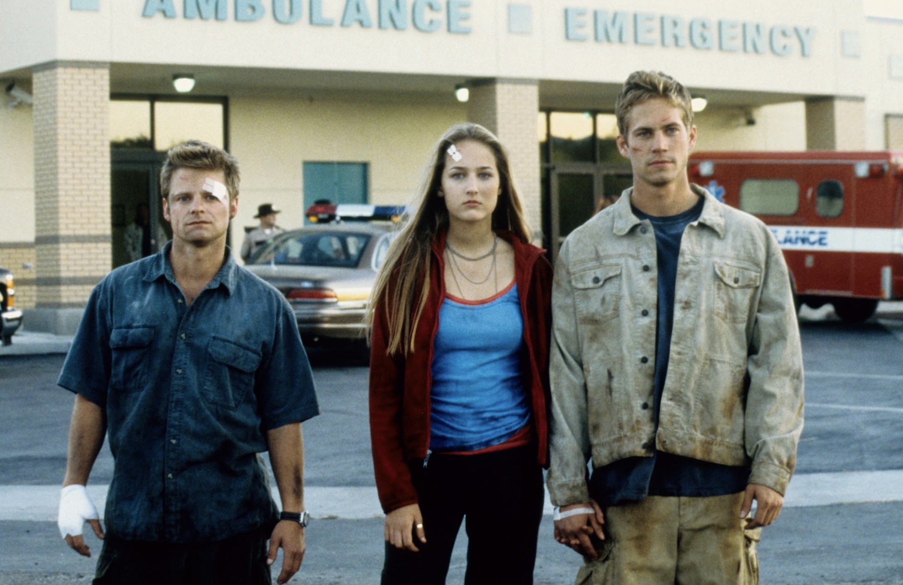 Trois personnes portant des bandages sur le corps se tiennent dans un parking.