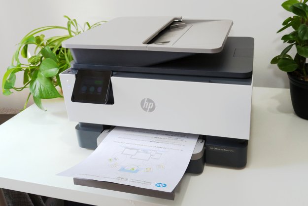 Der HP OfficeJet Pro 9125e steht auf einem weißen Ständer, umgeben von Pflanzen.