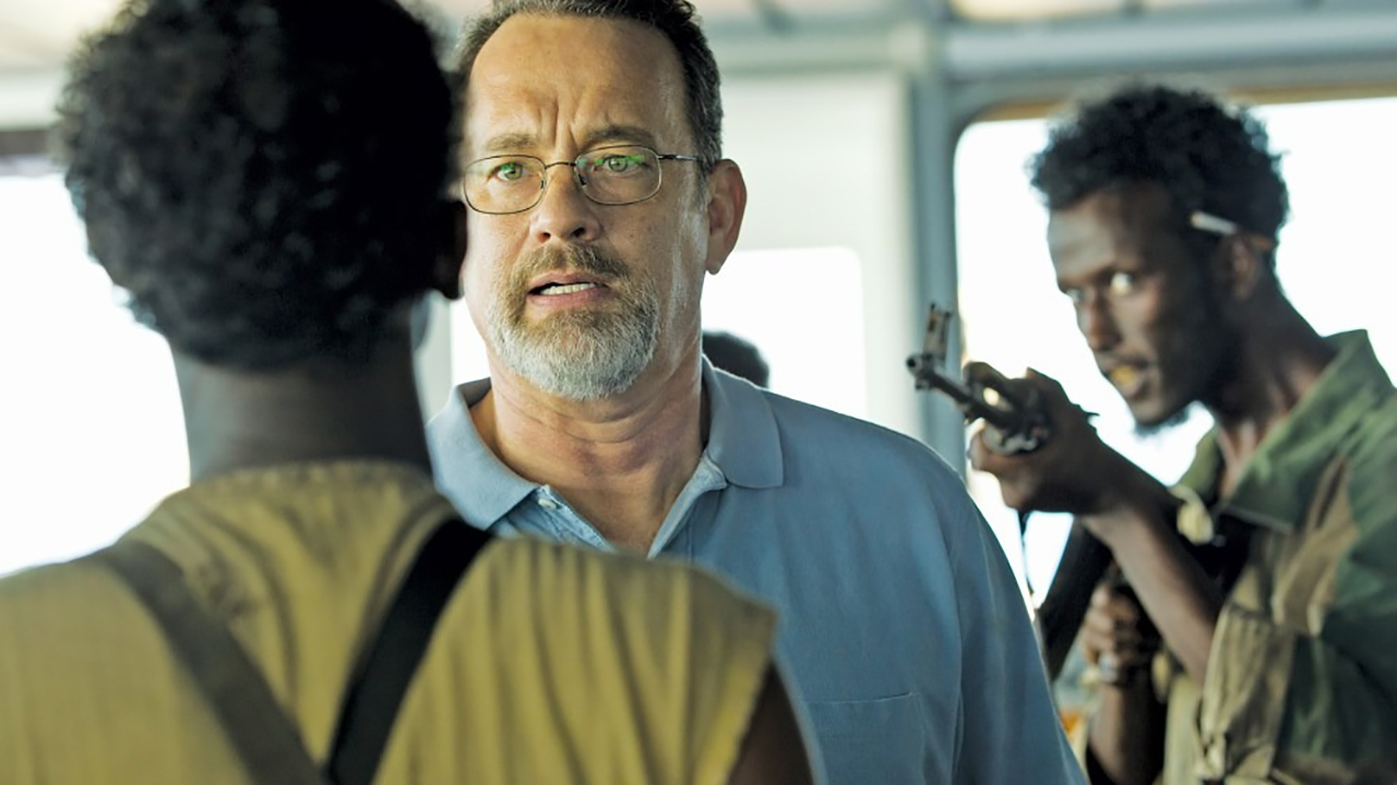 Tom Hanks con una pistola en la cabeza hablando con alguien en una escena del Capitán Phillips.