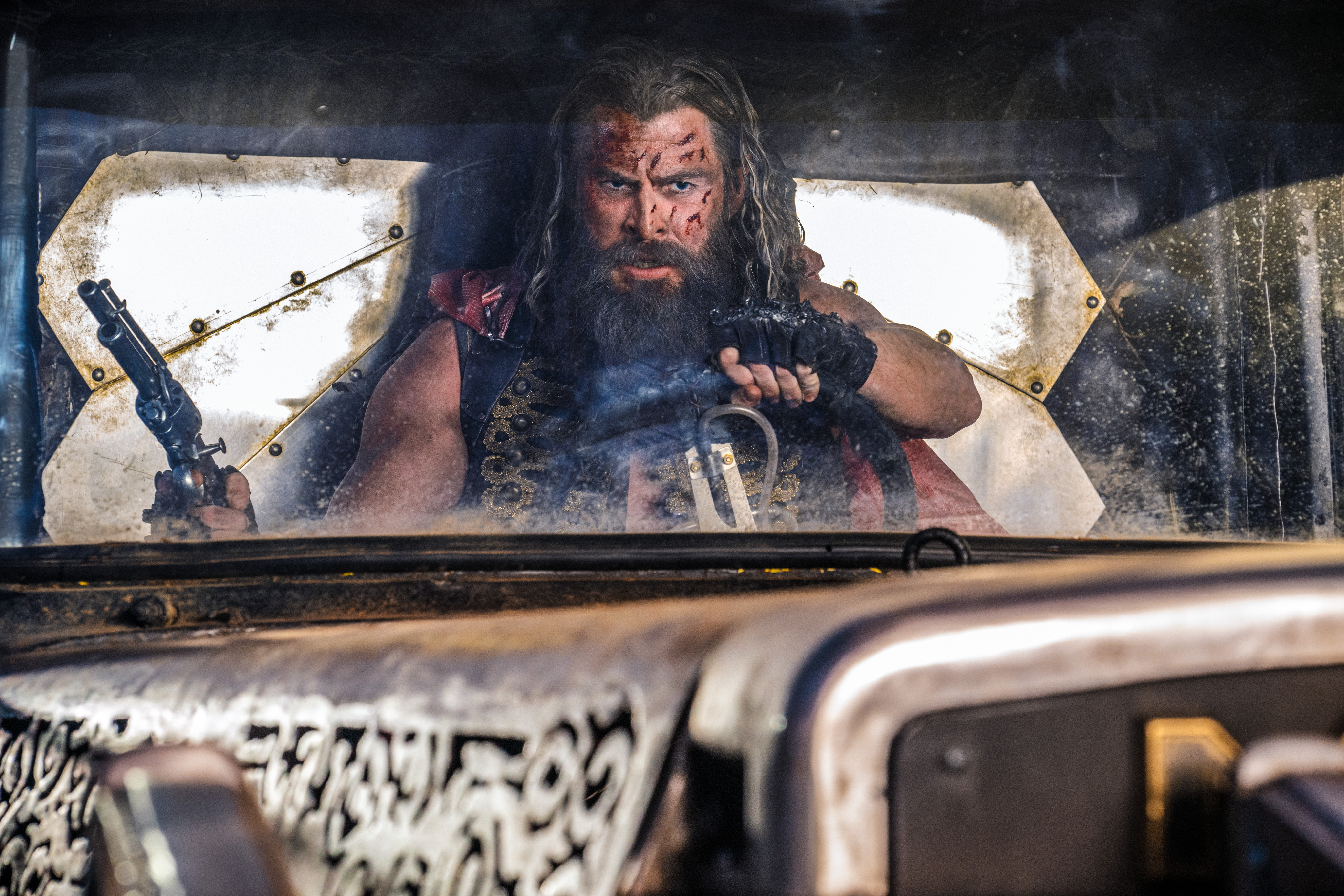 Un Chris Hemsworth ensangrentado sostiene una pistola y un volante en Furiosa: Una saga de Mad Max.