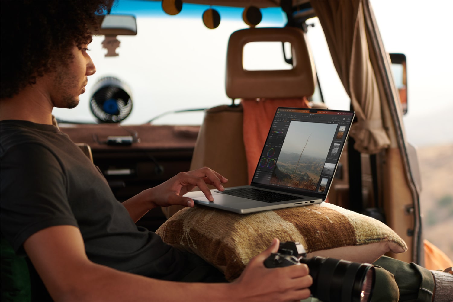 A person sitting in a vehicle using a MacBook Pro on their lap.