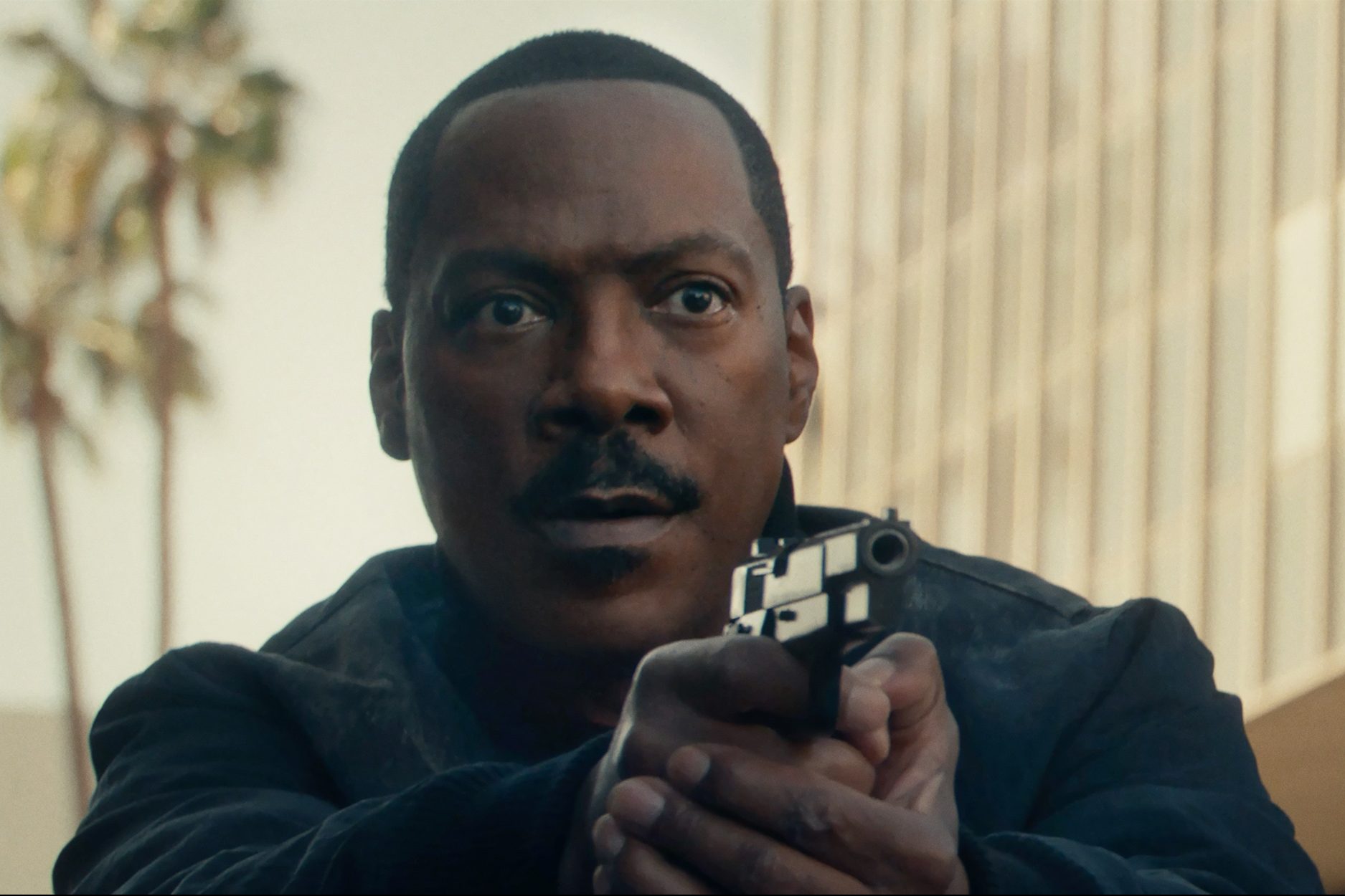 Eddie Murphy points a gun and cautiously stares.