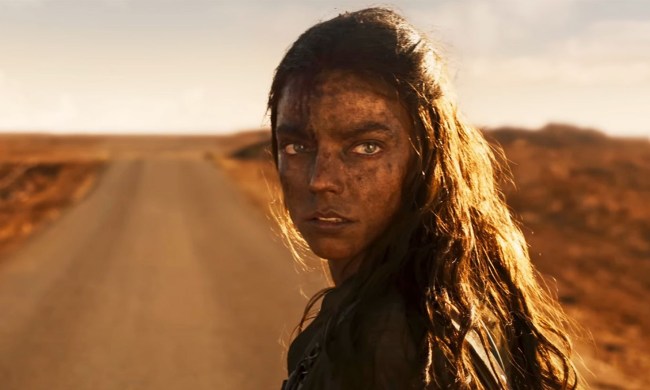 Anya Taylor-Joy stands on a dusty road and glances over her shoulder in a still from "Furiosa: A Mad Max Saga."