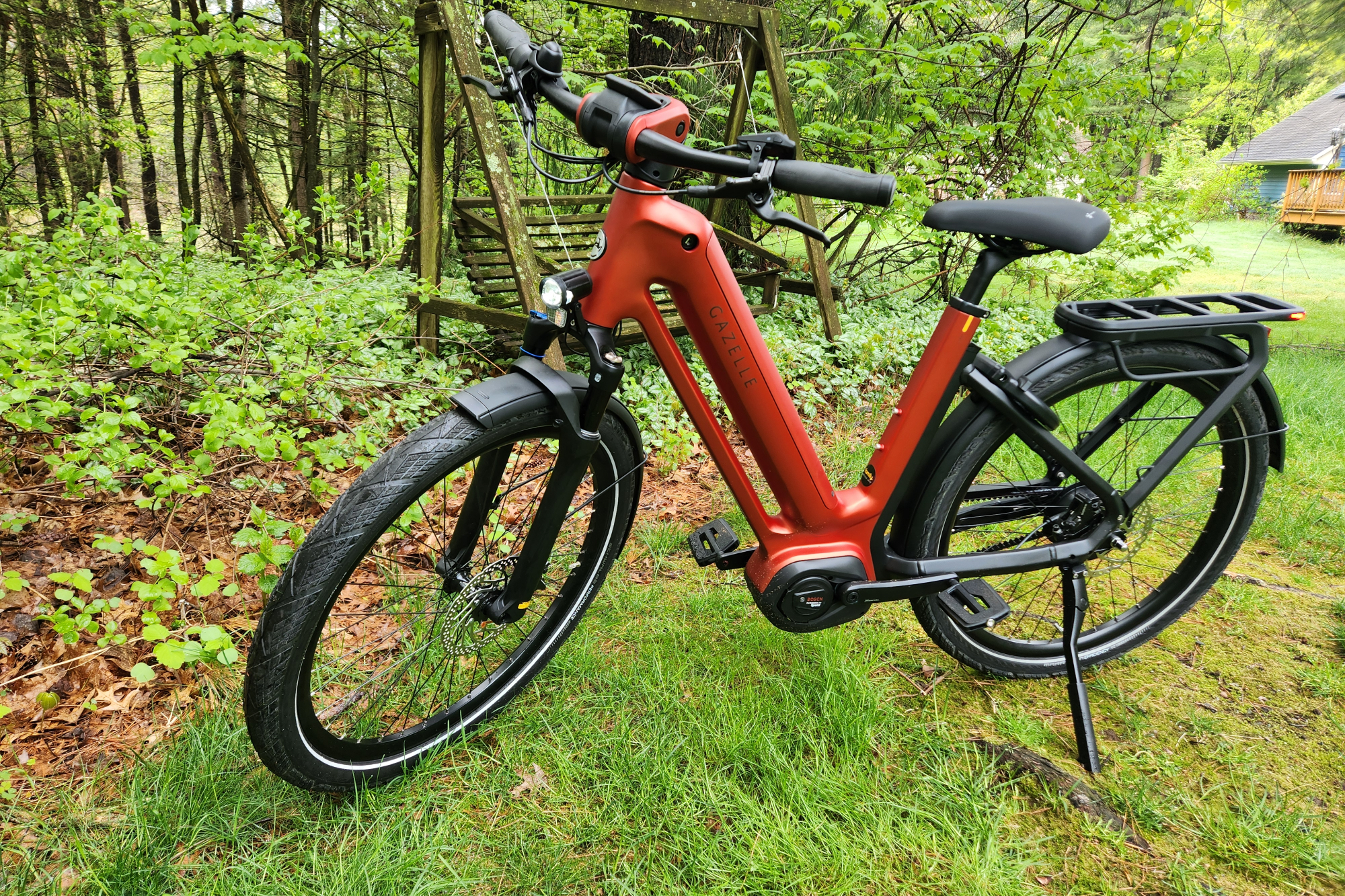 Vue de profil gauche du vélo électrique Gazelle Eclipse garé sur l'herbe avec des arbres et une vieille balançoire en arrière-plan.