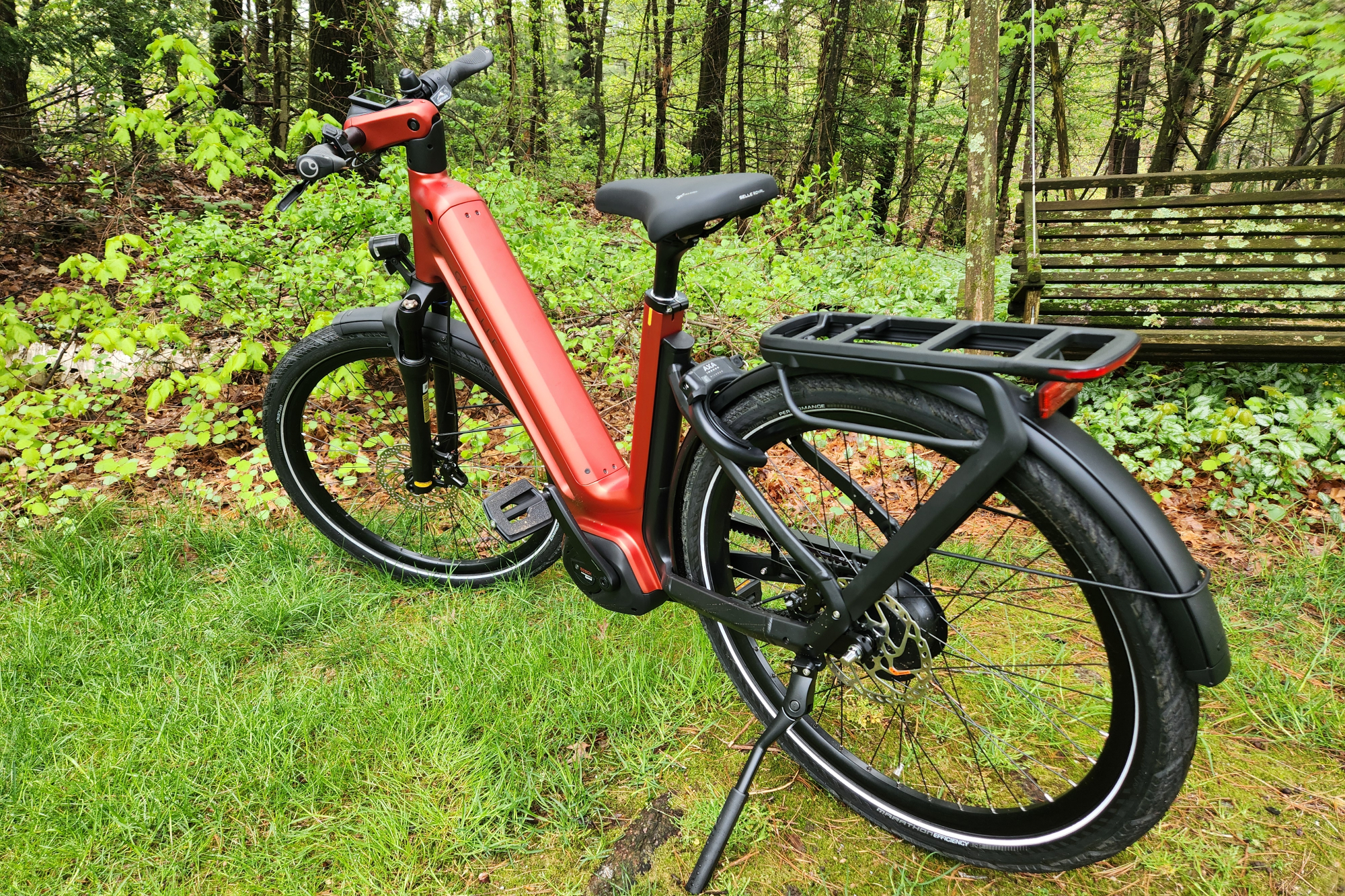 Vélo électrique Gazelle Eclipse, vue de trois quarts arrière gauche, garé sur de l'herbe avec des arbres et une vieille balançoire en arrière-plan.