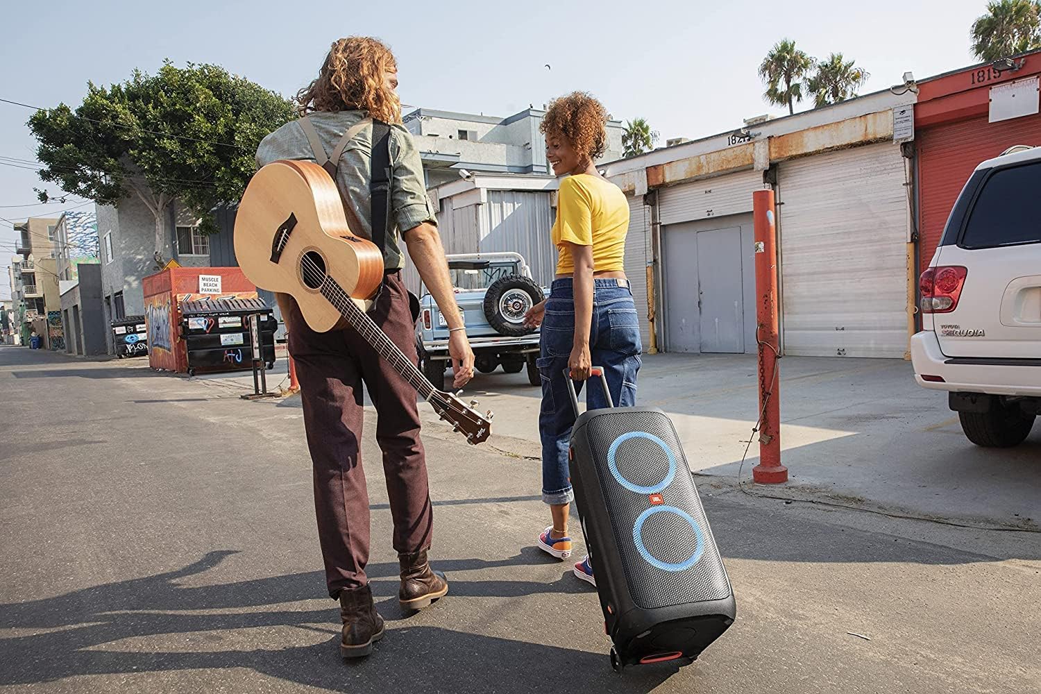 Duas pessoas caminhando por uma rua arrastando a JBL PartyBox 310 atrás delas.