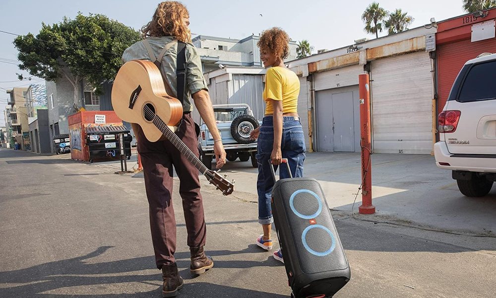 Two people walking along a street dragging the JBL PartyBox 310 behind them.