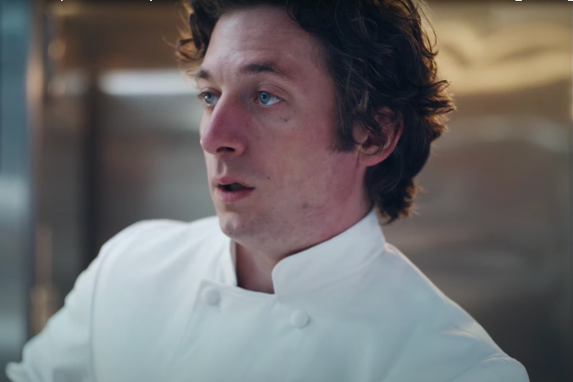 A man in a chef's coat looks to someone off-screen.
