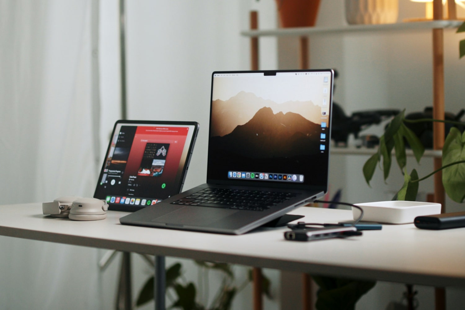Un iPad de Apple y un MacBook juntos en un escritorio junto a un par de auriculares.