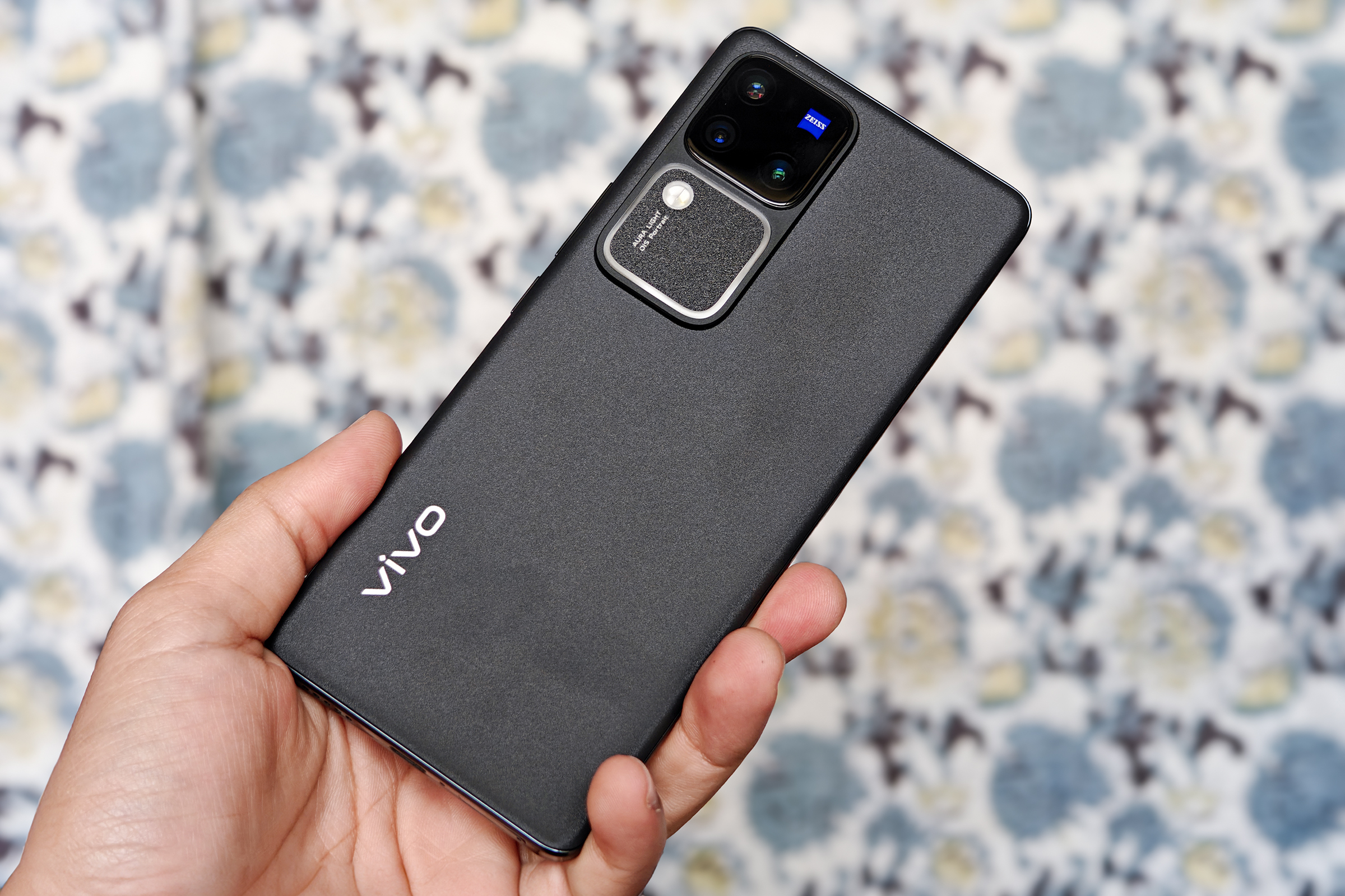 Gray Vivo V30 Pro with T* Zeiss lens coating held against a printed cloth.