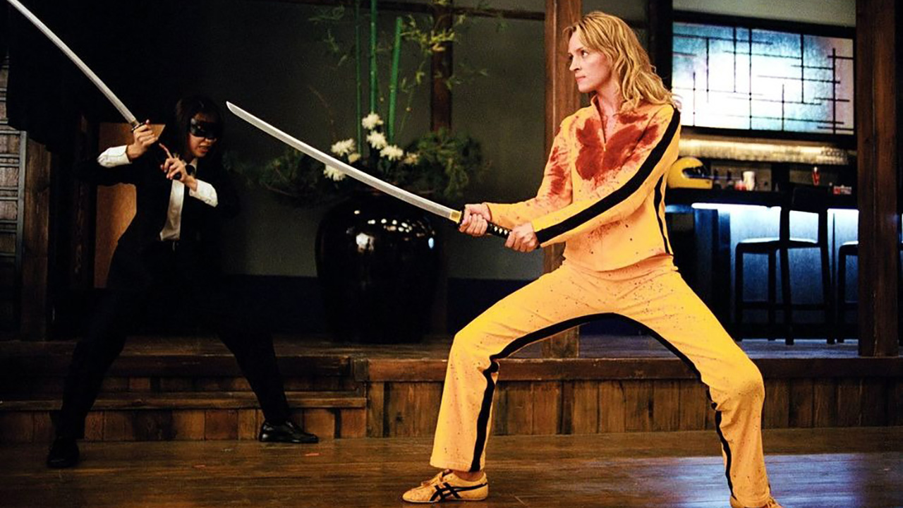 The Bride wielding a sword ready to fight a person in black, wearing a bright yellow outfit in Kill Bill: Vol. 1.