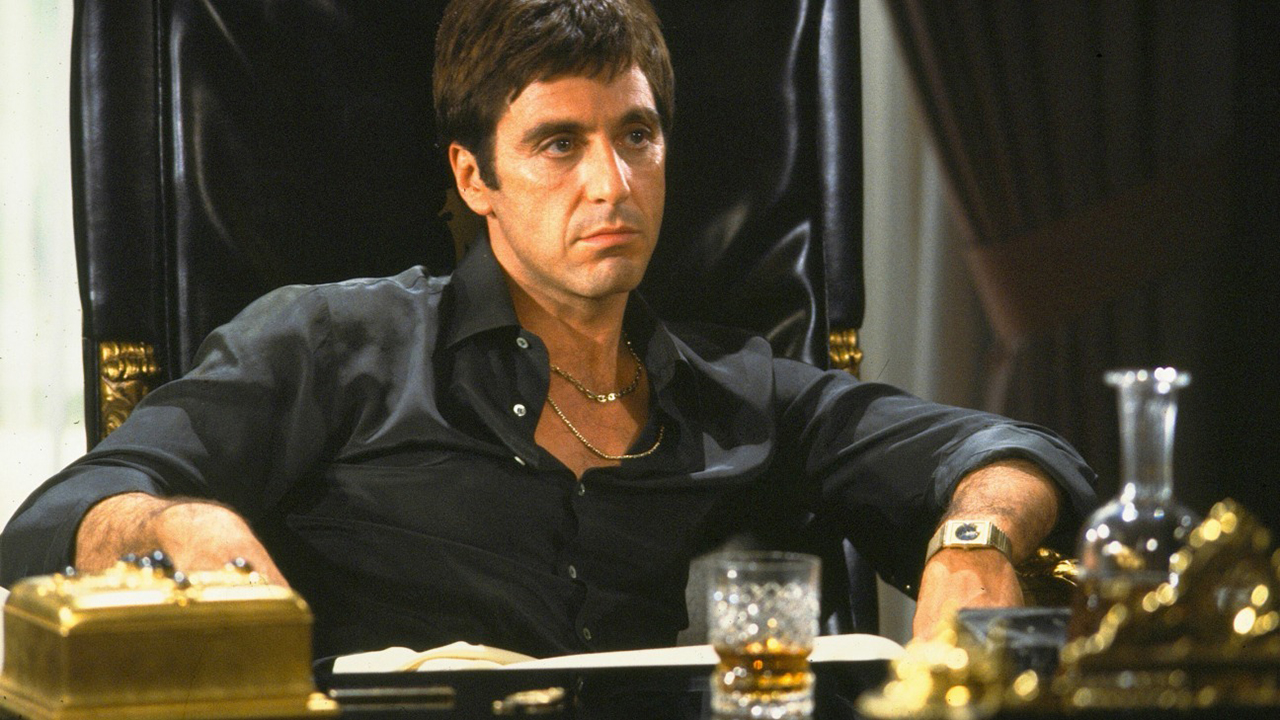 Al Pacino como Tony Montana en Caracortada sentado en su escritorio en una escena icónica.