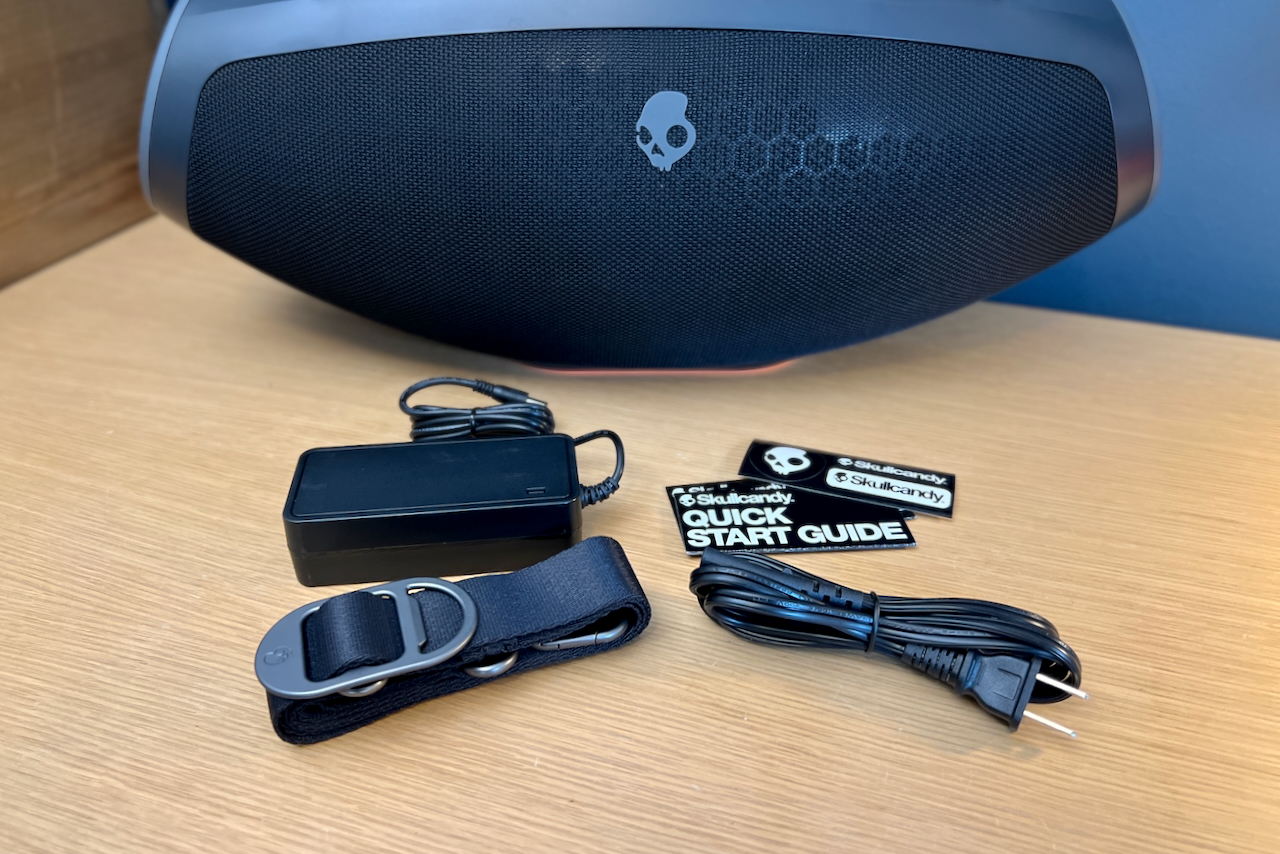 O alto-falante Bluetooth Skullcandy Barrel com sua alça e adaptador AC.