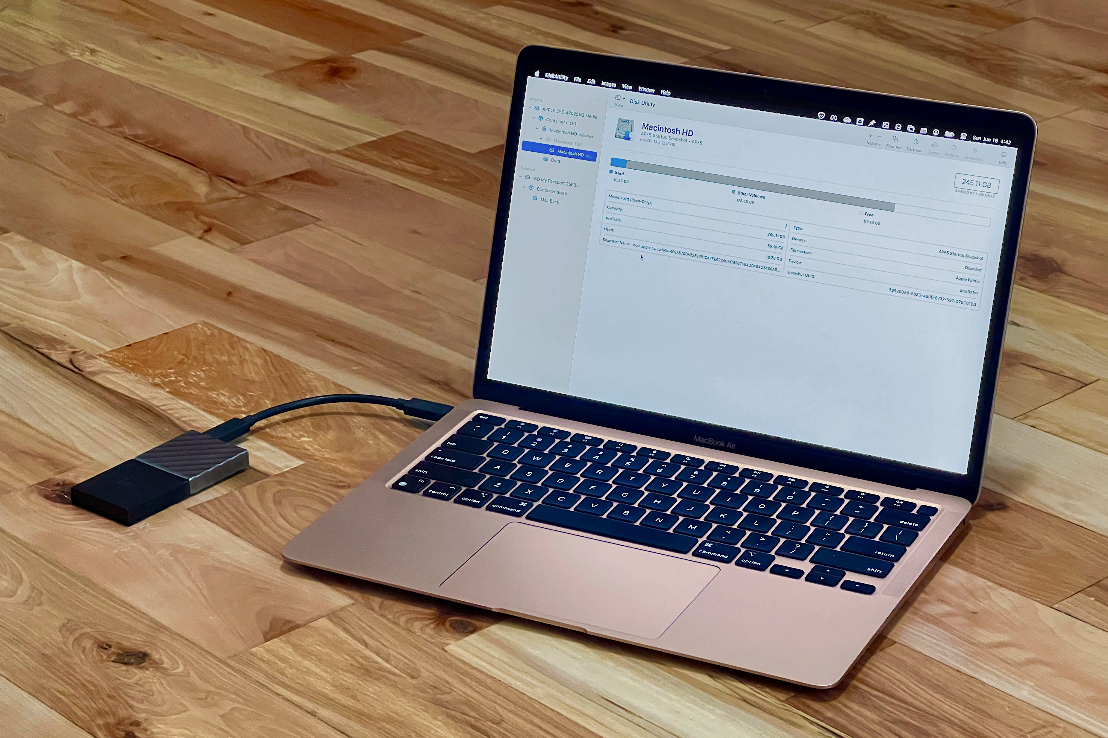 A rose gold MacBook Air has Disk Utility open and an external drive connected.