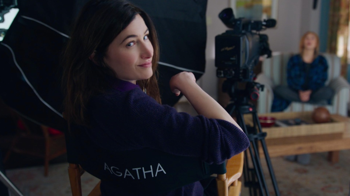 A woman sits in a director's chair and turns back to the camera.