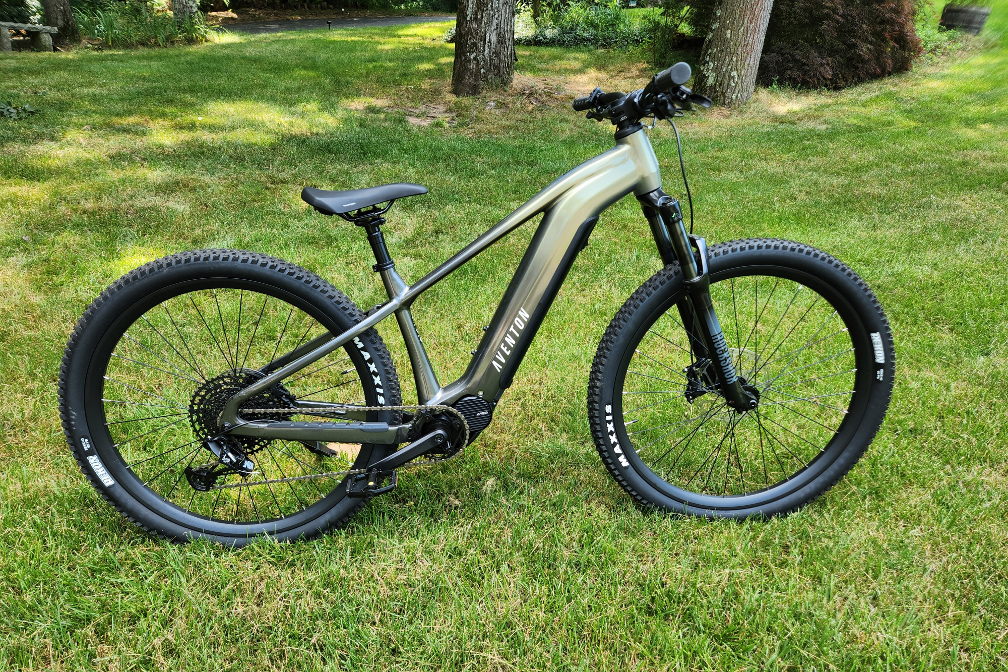 Правый профиль Aventon Ramblas eMTB на фоне травы, кустов и деревьев.