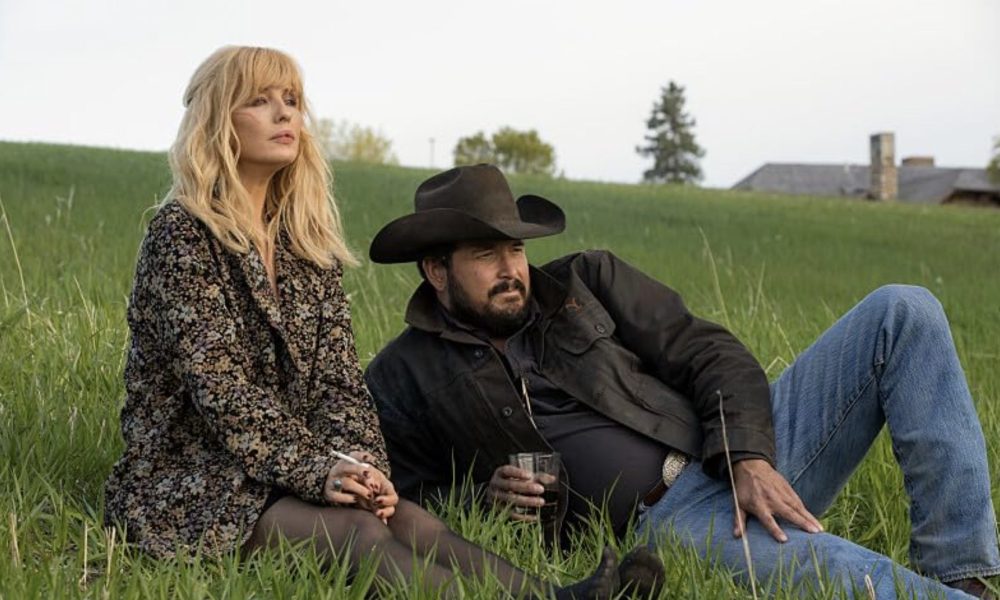 A woman sits down next to a man lying down on a hill.