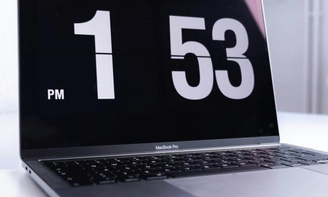 A MacBook Pro sitting on a desk with the time displayed on its monitor.