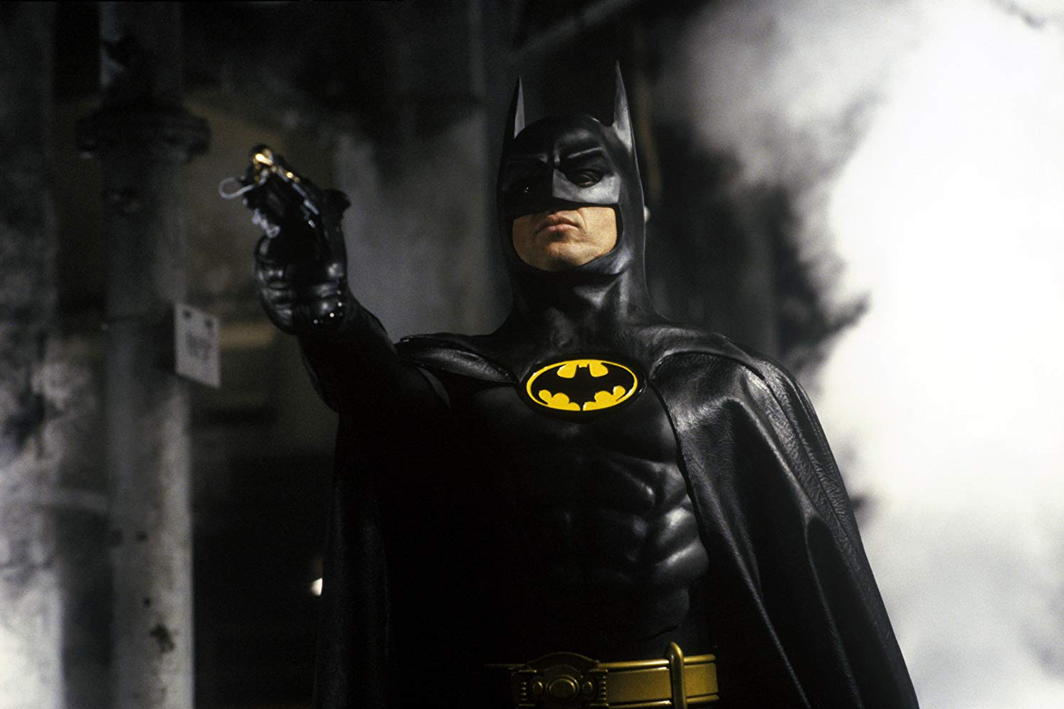 Michael Keaton points a grappling hook gun in Batman.
