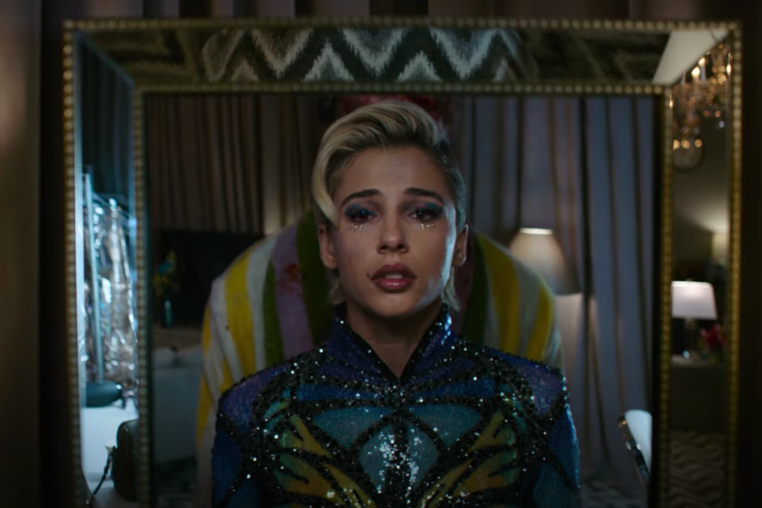 Una estrella del pop se ve triste mientras se mira en un espejo con alguien parado detrás de ella.