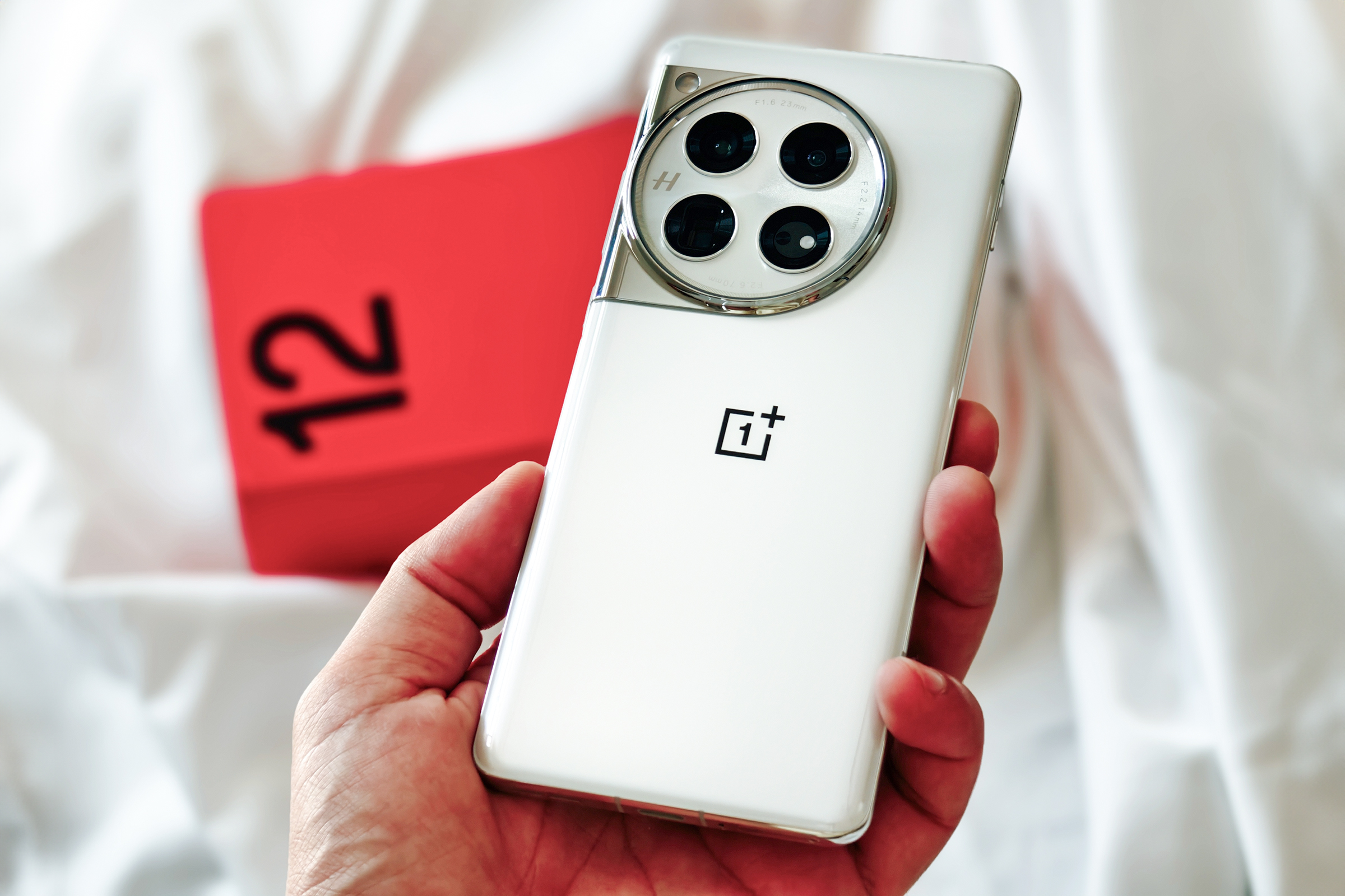 OnePlus 12 color Blanco Glacial sostenido en la mano contra su caja roja.
