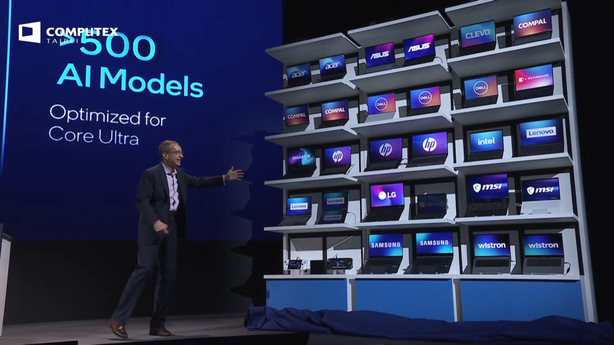 A wall of laptops at Computex 2024 with Intel CEO Pat Gelsinger standing next to them.