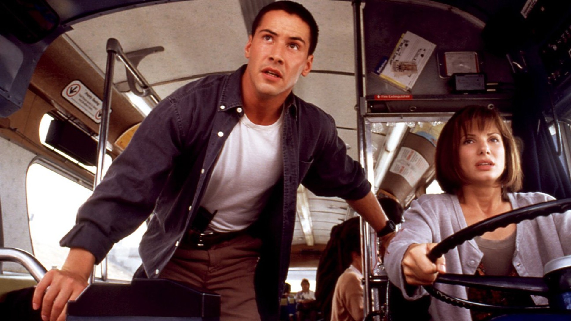 Keanu Reeves junto a Sandra Bullock mientras conduce un autobús en una escena de la película Speed