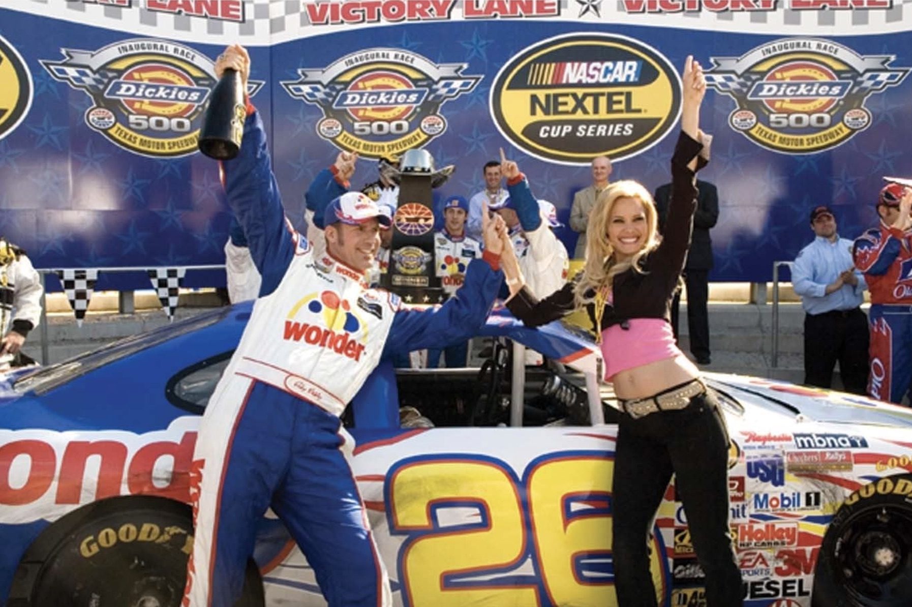 A racing driver parties with a woman in front of a racing car.