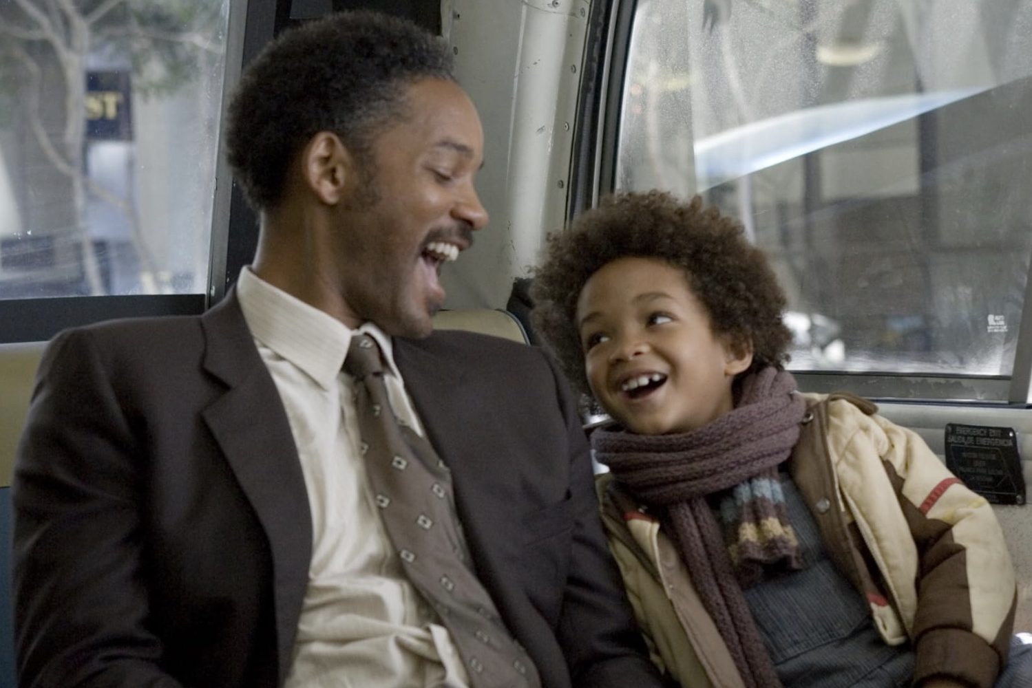 Un hombre en un asiento de autobús se ríe con su hijo sentado a su lado.